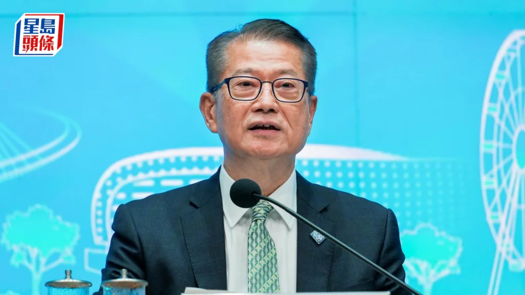 財政司司長陳茂波身穿西裝及領帶，在印有香港地標圖案的佈景板前發言。