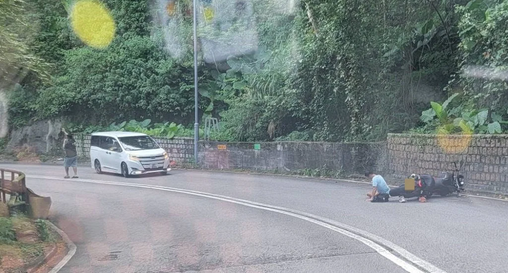 荃錦公路彎位有一輛電單車倒臥路邊，有路人在旁協助。