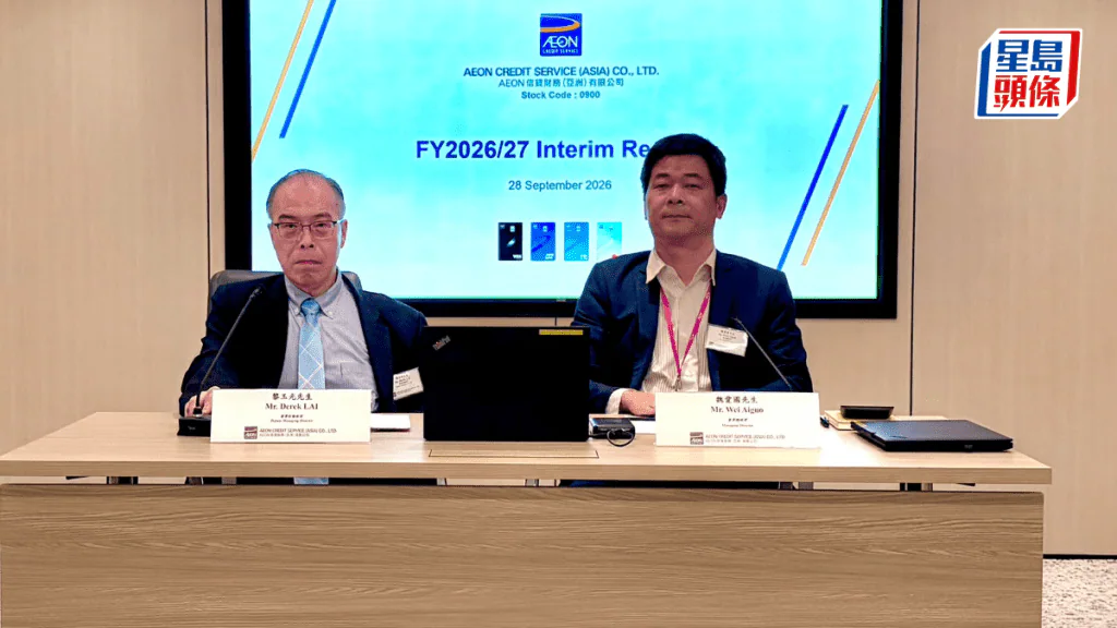 AEON信貸財務舉行中期業績發布會，會議桌上放置寫有賴先生及森下先生的名牌，後方屏幕顯示公司名稱及中期業績標題。