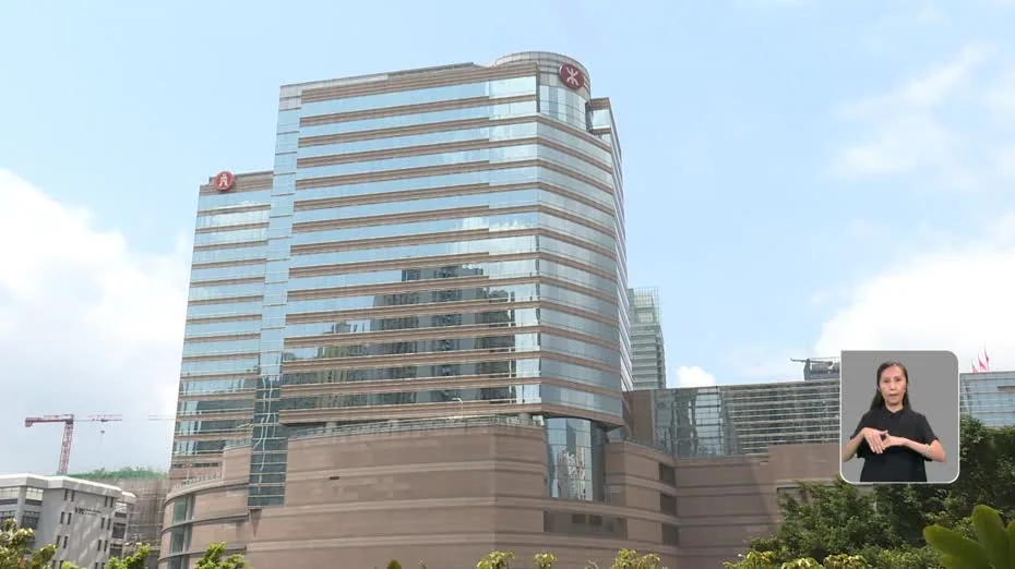 位於九龍灣的港鐵總部大樓外觀，右下角設有手語傳譯視窗，顯示一名人士正進行手語傳譯。