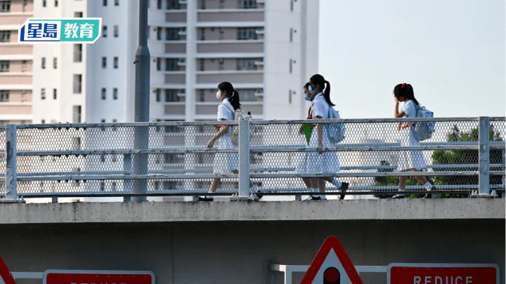 四名身穿校服的學生行走在行人天橋上，背景為住宅大廈，反映本港中學學額調整後的校園生活面貌。