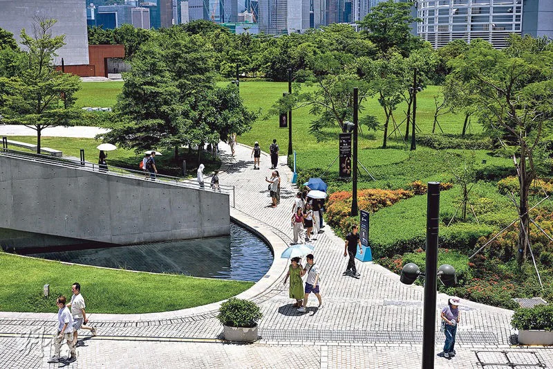西九文化區藝術公園的戶外環境，設有行人路、草地及水池，背景為香港城市建築群。