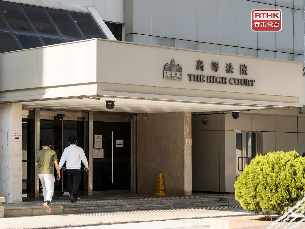 兩名身穿便服的男子步入香港高等法院大樓，大樓入口上方掛有「高等法院」及「THE HIGH COURT」的中英文招牌。