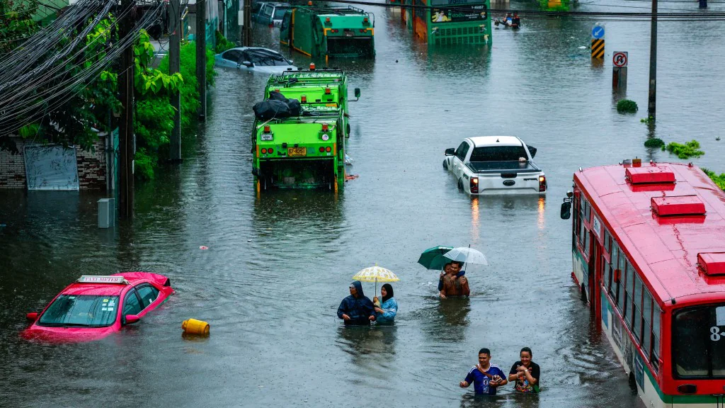 曼谷街道嚴重水浸，多輛汽車及巴士被困水中，市民在積水中步行，部分人撐傘前行，現場環境顯示暴雨造成的災情。