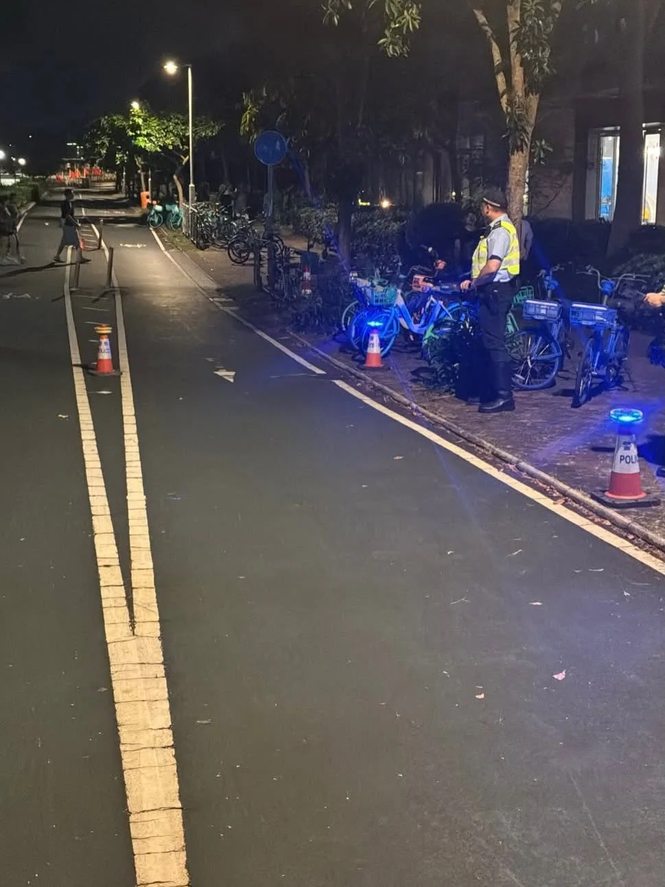 將軍澳警區警員在夜間的單車徑旁進行執法行動，現場停泊多輛單車並放置閃爍藍燈的交通錐。