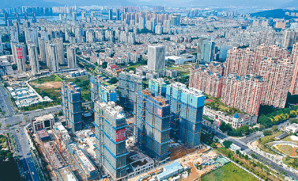 高空俯瞰城市景觀，可見多棟正在興建中的住宅大廈，外牆被藍色防護網覆蓋。