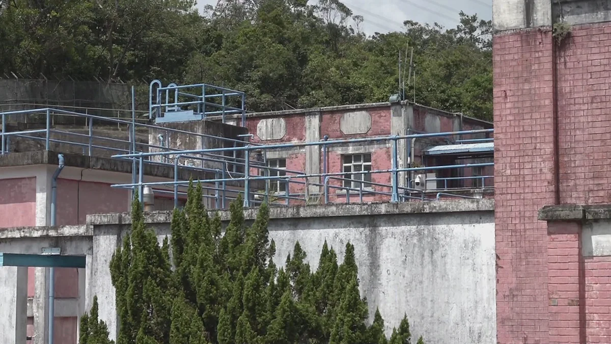 金山石梨貝濾水廠外觀，紅磚建築物周邊設有藍色欄杆及圍牆，背景為樹木。