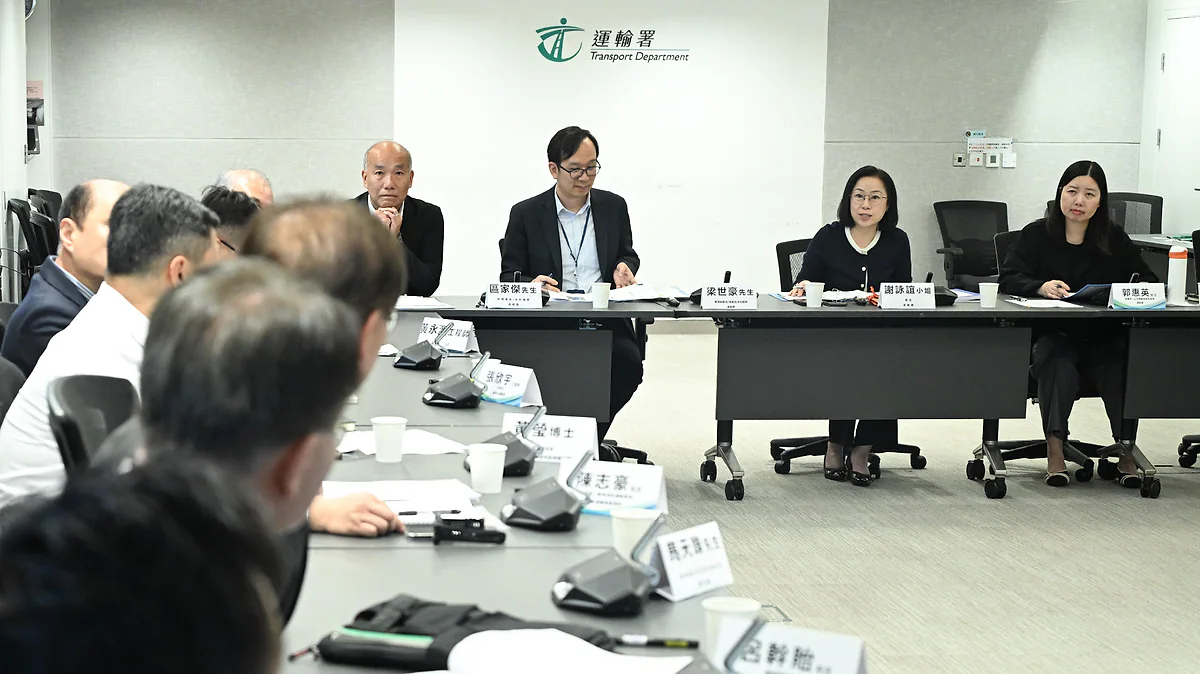 運輸署自動駕駛車輛應用促進工作組舉行會議，多名與會者圍繞長形會議桌就座，背景牆上印有運輸署標誌。