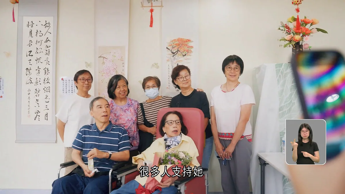 黃慧明在白普理寧養中心舉辦的個人畫展中，與親友及醫護人員合照，現場展示了多幅書法及畫作。
