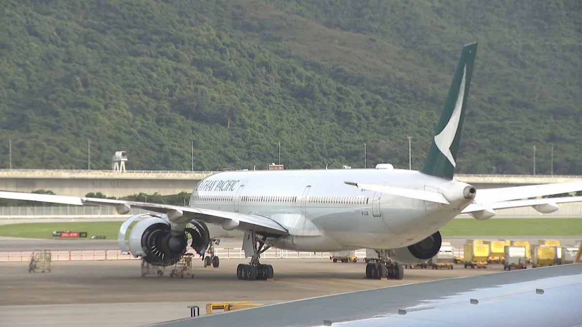 停泊在機場停機坪上的國泰航空客機，機身印有國泰航空標誌，背景為綠色山坡。