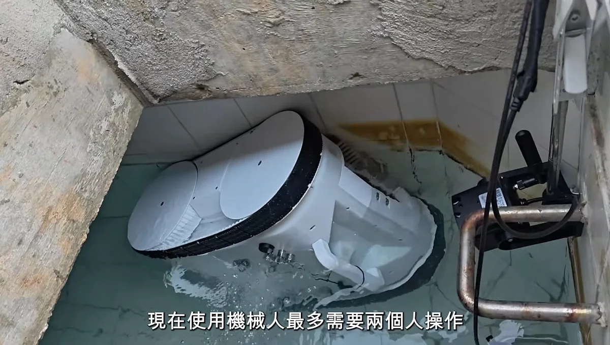 白色洗水缸機械人於密閉水缸內進行清潔作業，操作人員透過遙控器及實時鏡頭監控其運作狀態。