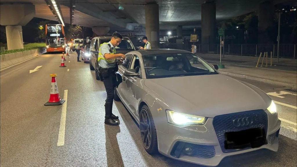 警務人員於夜間路邊截停一輛灰色私家車，並向司機檢查證件以進行交通違例執法。