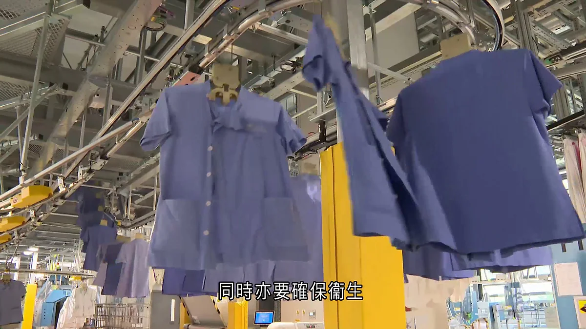 醫院管理局支援服務中心內的自動化輸送帶系統，正運送多件已清洗的藍色制服，確保衣物處理過程的衛生與效率。