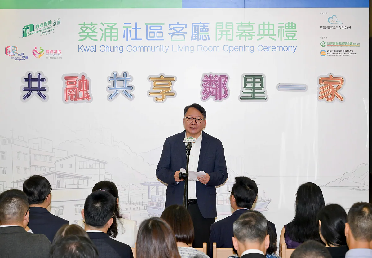 政務司司長陳國基在葵涌社區客廳開幕典禮上致辭，現場背景印有「共融共享鄰里一家」的主題字樣。