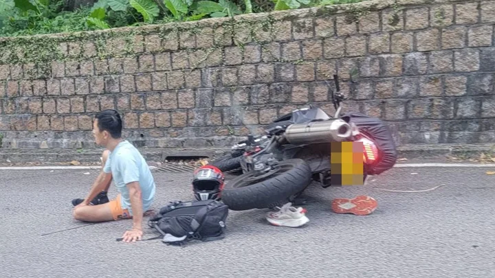 電單車在荃錦公路路邊倒地，一名男子坐在旁邊，身旁放有頭盔及背囊。