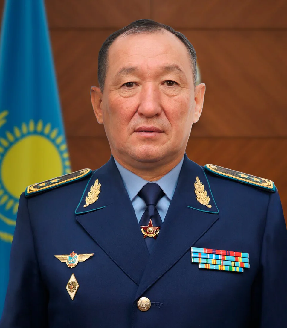 哈薩克國防部長科薩諾夫身穿深藍色軍服，背景為哈薩克國旗。