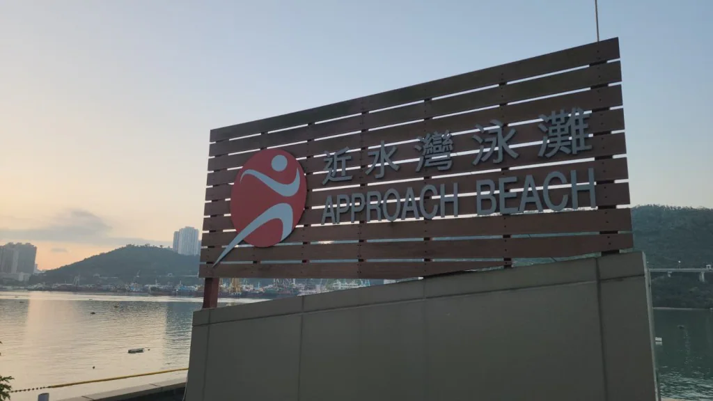 荃灣近水灣泳灘入口指示牌，背景可見海面及遠處山景。