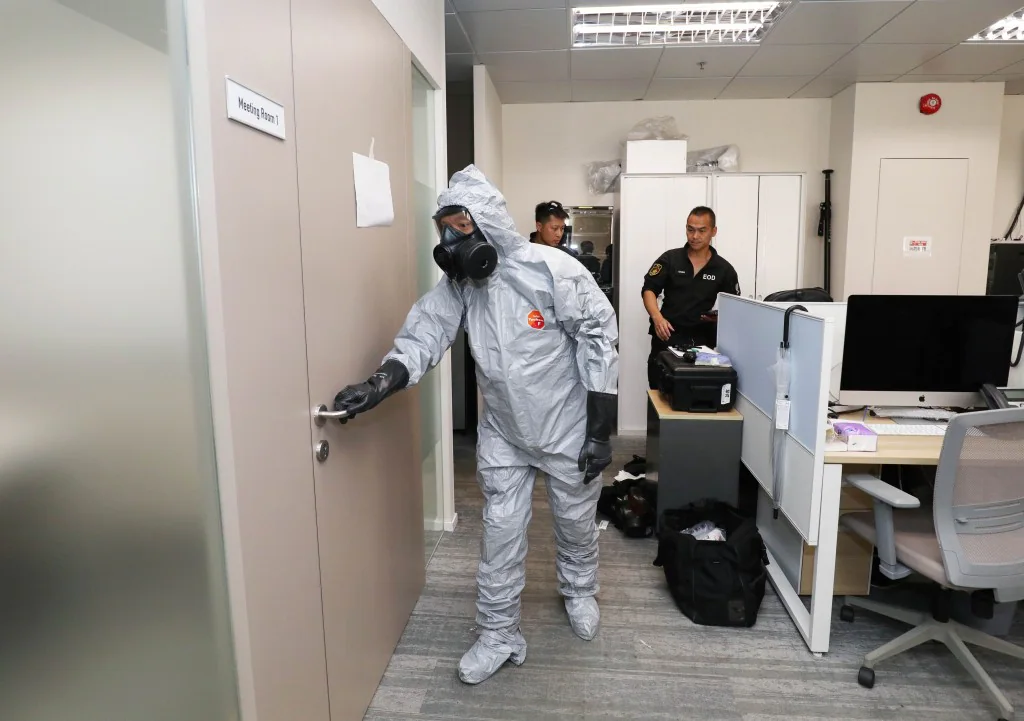 身穿保護衣及佩戴防毒面具的爆炸品處理課人員，在辦公室內準備檢查涉事證物。