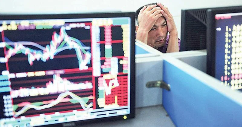 一名男子坐在電腦螢幕前雙手抱頭，螢幕顯示多條呈現下跌趨勢的股市走勢圖。